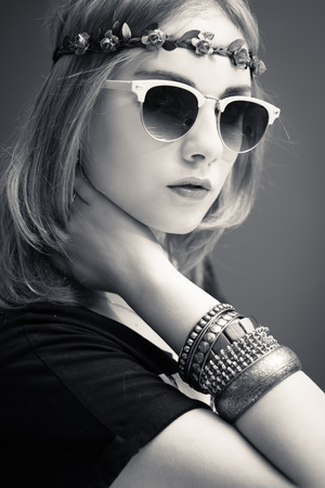 Studio black and white portrait of teenage hipster or hippie girl wearing trendy flower wreath and sunglasses over copy space backgroundの写真素材