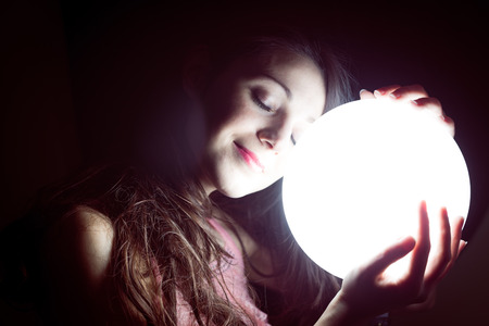 closeup image of beautiful young sleeping woman holding ball of light and happy smilingの写真素材