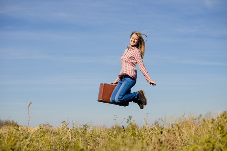 Funny happy teenage girl jumping with retro suitcase over blue sky copy space backgroundの写真素材