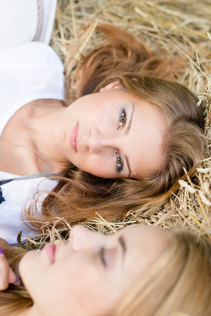 closeup picture of 2 beautiful young women best friends having fun relaxing lying on hay stackの写真素材