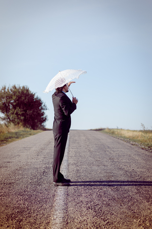 Rear view of man with white umbrella looking away on the roadの写真素材