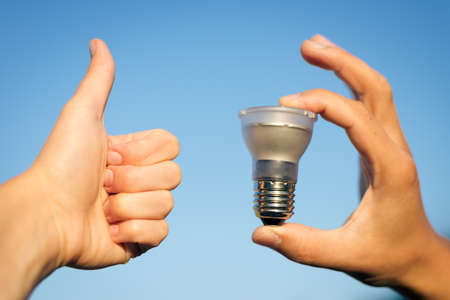 LED lamp in hand and thumb up against blue sky