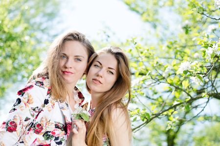 Two young pretty girls standing under blooming tree