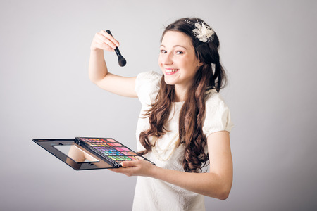 Pretty young woman applying make-up and looking at cameraの写真素材