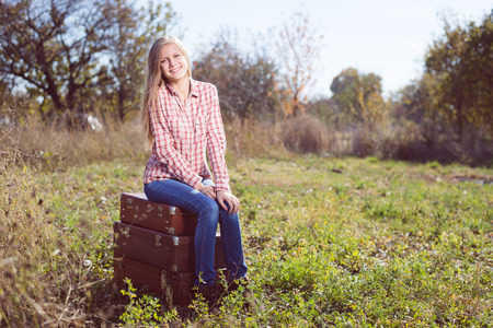Funny happy teenage girl sitting on retro suitcases over field backgroundの写真素材