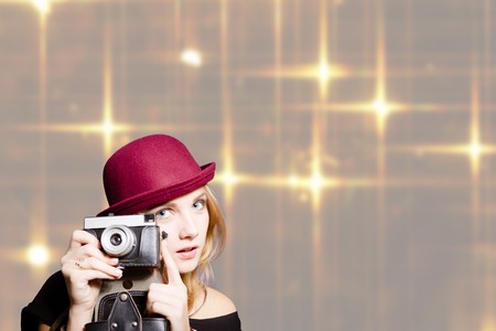 Portrait of pretty girl in hipster glasses and pot hat holding vintage camera. Young woman happy smiling on bright shiny bokeh background.の写真素材