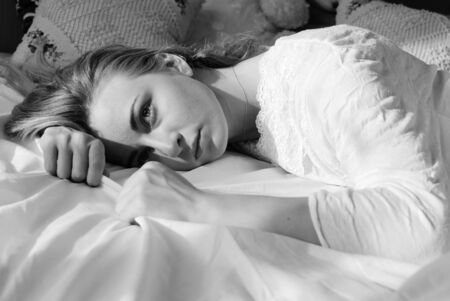 black and white picture of emotional beautiful blond young woman relaxing lying in bed looking at copy space on bedroom background closeup portraitの写真素材
