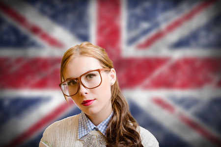 Portrait of beautiful young woman in big glasses and sweater. Student girl on english Union Jack blurred background.の写真素材