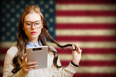 Picture of pretty girl in big hipster glasses with ebook. Young student reading on USA flag blurred background.の写真素材