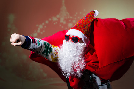 Picture of funny Santa Claus wearing heart shape sunglasses and red coat flying like super man to be in time on bright festive bokeh backgroundの写真素材