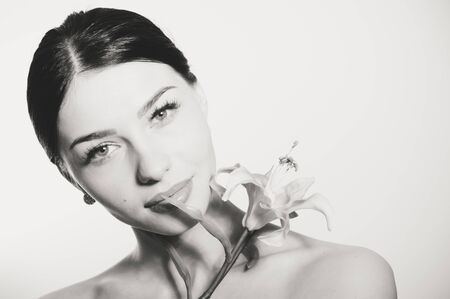 Black and white portrait of a beautiful lady looking at camera face with red lipstick and lillies flower. Perfect skin.の写真素材