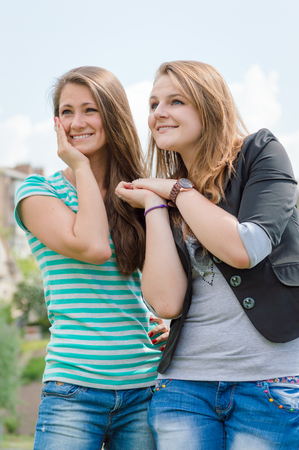Friendship concept. Two smiling girls over blue skype outdoors backgroundの写真素材
