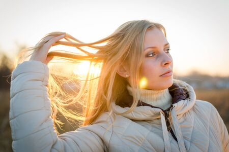 Portrait of a beautiful young woman with blond hair. Shot outdoors in a cold autumn day with natural background.の写真素材