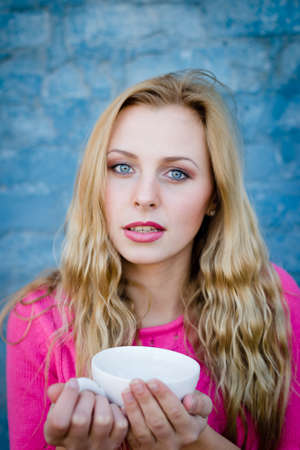 Coffee break. Portrait of happy amazed beautiful young lady holding cup of beverage over blue copy space backgroundの写真素材