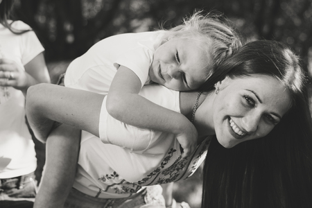 Beautiful young woman carries on her back little girl and happy smiling outdoors black and white pictureの写真素材