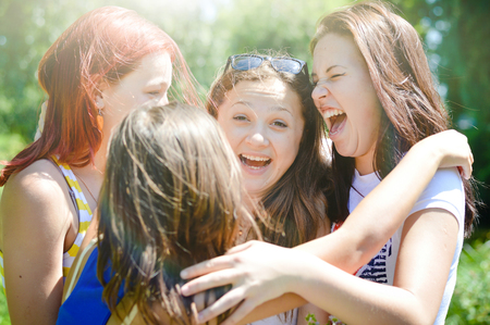 Four happy female friends hugging in green summer park sun light outdoors backgroundの写真素材