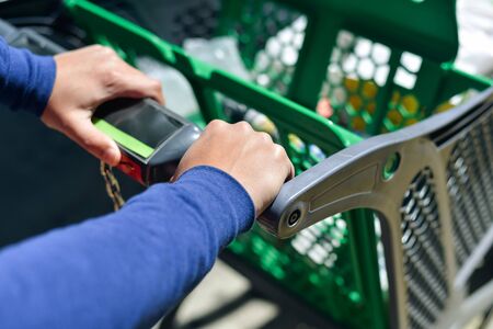 Closeup picture of male hand holding shopping push cart on car parking