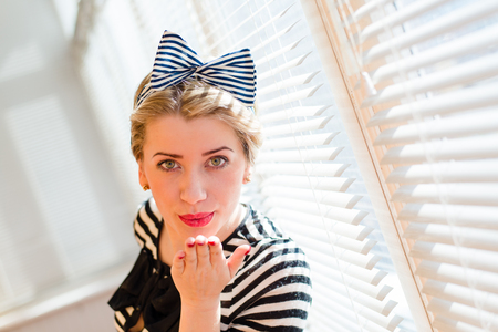 Closeup picture of beautiful blond young woman pinup girl having fun happy smiling and looking excited at the sun lighted windowsの写真素材