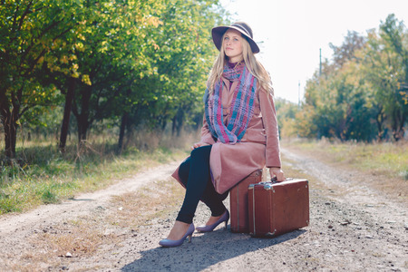 Woman alone with vintage suitcase hitchhiking on empty road outdoors. Travel abroadの写真素材