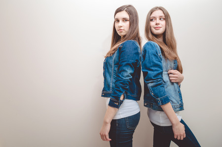 Closeup portrait of two beautiful young women with long dark hair and natural makeup wearing jeans shirts happy smiling looking at cameraの写真素材