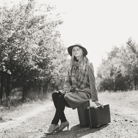 Black and white portrait of woman alone with vintage suitcase hitchhiking on empty road outdoors. Travel abroadの写真素材
