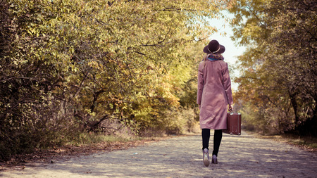 Portrait of woman in hat and coat with suitcase on the road outdoors backgroundの写真素材