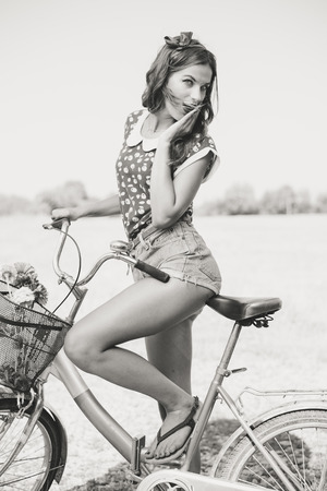 Black and white portrait of young beautiful brunette pinup woman cycling in counrtyside landscape summer copy space imageの写真素材