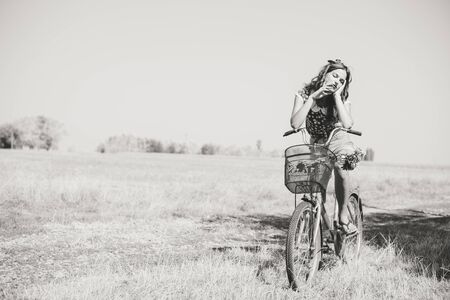 Black and white image of young beautiful brunette pinup woman sexy lady holding bicycle on countryside summer background copy space portraitの写真素材