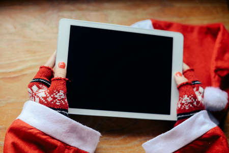 Woman's hand with red wool glove with tablet pc on wood background ready for Christmasの写真素材