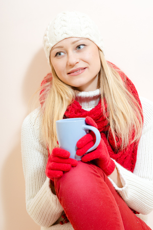 Red hat and cup: portrait of pretty girl in knitted gloves and cap with a pattern snowflakes, white sweater having fun drink beverage happy smiling and looking at camera on light copy space backgroundの写真素材