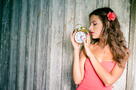 Portrait of attractive young lady having fun holding alarm-clock on wooden copy space backgroundの写真素材