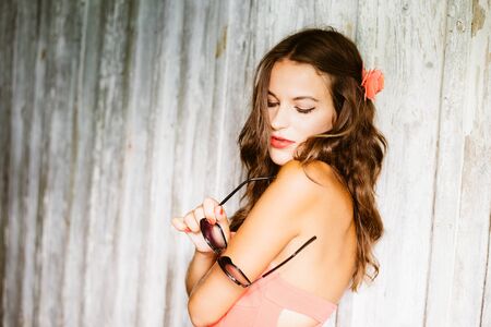Sexy glamor attractive brunette woman fashion model holding sunglasses in hand, portrait over old barn wood wall backgroundの写真素材