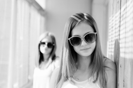 Black and white picture of 2 best girl friends or sisters playful in sun glasses. beautiful blond young women having fun posing happy smiling and looking at camera on sun lighted windows backgroundの写真素材