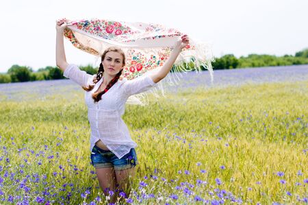 Young smiling happy woman standing in yellow summer wheat field holding a white shawl in the windの写真素材