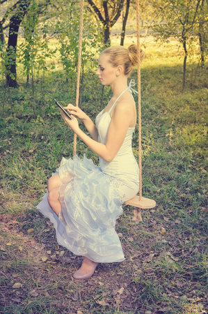 Happy positive attractive blond woman using tablet pc on summer day outdoors backgroundの写真素材
