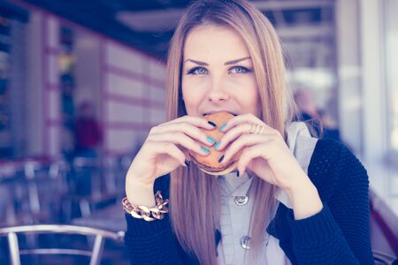 Pretty woman with hands holding fast food burger on restaurant background, mockup space for text message or design. closeup portrait viewの写真素材