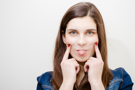 Young attractive caucasian stylish woman wearing blue jeans jacket and showing tongue on studio background. Closeup portrait, trendy lifestyleの写真素材