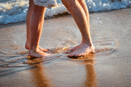 Holiday vacation. Loving couple walking, hugging and kissing on the beach at sunset. Two lovers, man and woman barefoot near the water. Summer in love, natural outdoors backgroundの写真素材