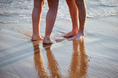 Holiday vacation. Loving couple walking, hugging and kissing on the beach at sunset. Two lovers, man and woman barefoot near the water. Summer in love, natural outdoors backgroundの写真素材