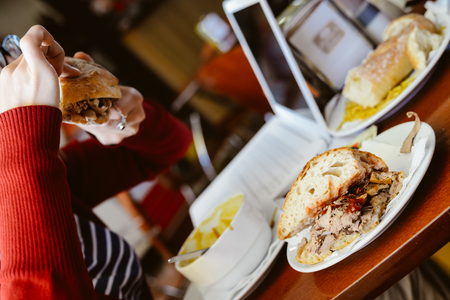 Closeup of female eating and working on laptop computer, wooden table background. Modern meeting busy communication lifestyle conceptの写真素材