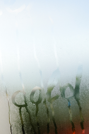 Cold sign on wet drops window glass during cool season natural blurred textured background. Close up view of fresh condensate and written word on shiny ripple droplet foggy blur reflectionの写真素材