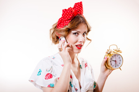 Closeup portrait of pinup woman with alarm clock speaking on mobile phoneの写真素材