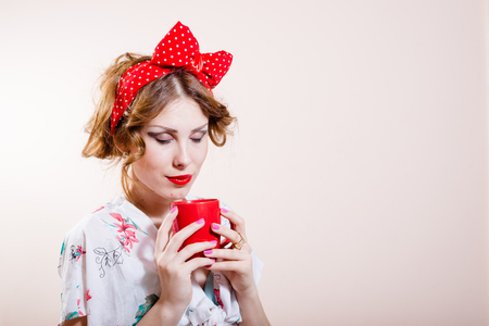 closeup portrait on beautiful funny pinup blond young woman with red lips having fun drinking tea happy smiling looking at camera and showing biceps muscles on white background pictureの写真素材