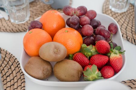 Fresh mixed tropical fruit kiwi, orange, grapes, strawberry on white plate for breakfast