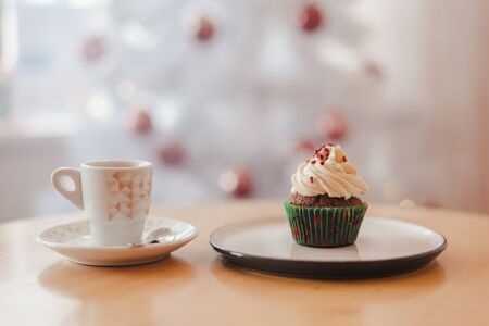 Italian coffee Cup and cupcake on the table near the white Christmas tree with golden bokehの写真素材
