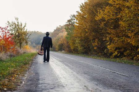Lonely guitarist looking at empty country road in autumn.の写真素材