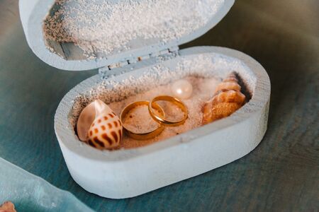 wedding rings in a rustic box with white sand and seashells, for the wedding ceremony or vow renewalの写真素材
