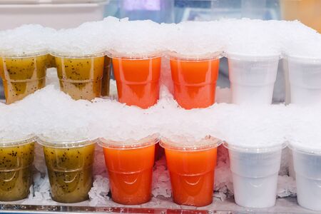 Fruit smoothy juice mix with ice arranged in plastic cups on a market stall with small fork inside, takeaway healthy snackの写真素材
