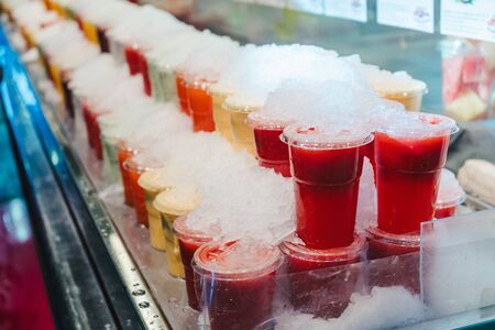 Fruit smoothy juice mix with ice arranged in plastic cups on a market stall with small fork inside, takeaway healthy snackの写真素材
