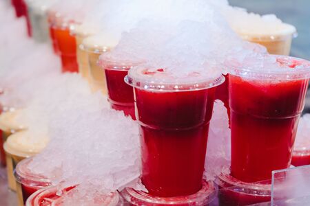Fruit smoothy juice mix with ice arranged in plastic cups on a market stall with small fork inside, takeaway healthy snackの写真素材
